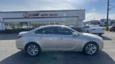 Silver sedan parked in front of a car dealership with a white building that reads 'E-Z LOAN AUTO SALES' and multiple cars in the lot behind it, under a clear blue sky.