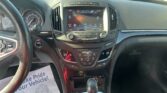 Interior view of a car showing the center infotainment touchscreen, climate controls, and gear shifter, with a parking lot outside the windshield.
