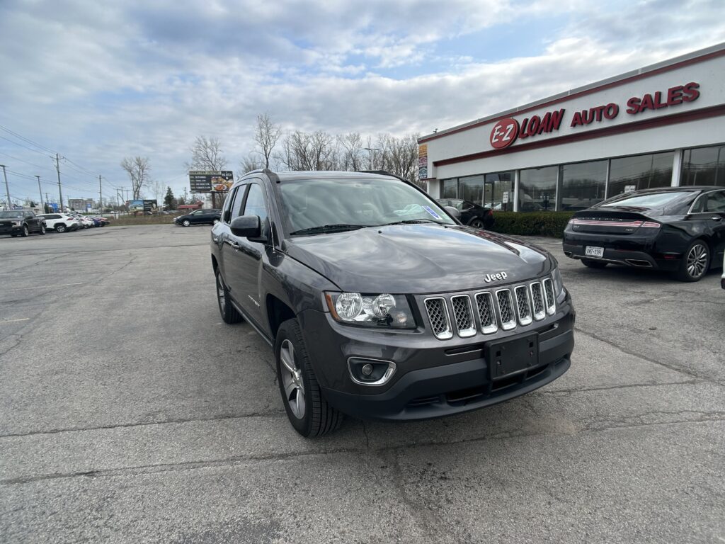 Front-left angle of a dark gray Jeep SUV in a car lot near an E-Z Loan Auto Sales storefront under a cloudy sky.