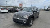 Front-right view of a gray Jeep SUV in a car dealership parking lot, with other vehicles and an EZ Loan Auto Sales sign in the background under a cloudy sky.