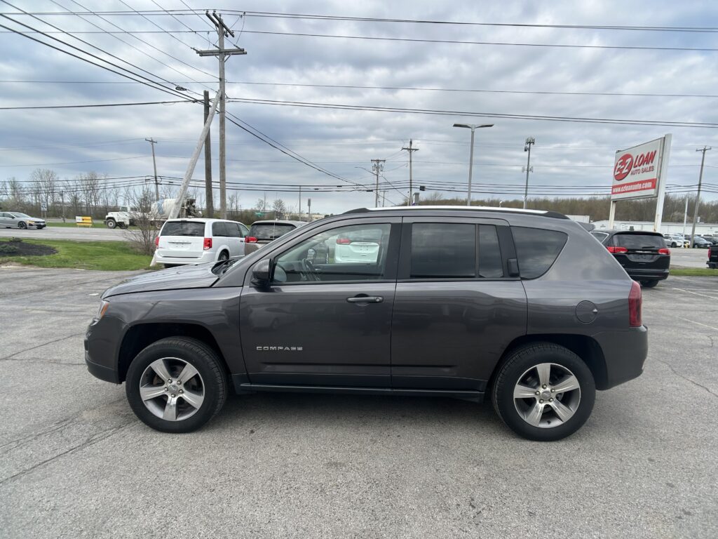 Gray Jeep Compass SUV in a car dealership lot, with other vehicles and an EZ Loan Auto Sales sign in the background