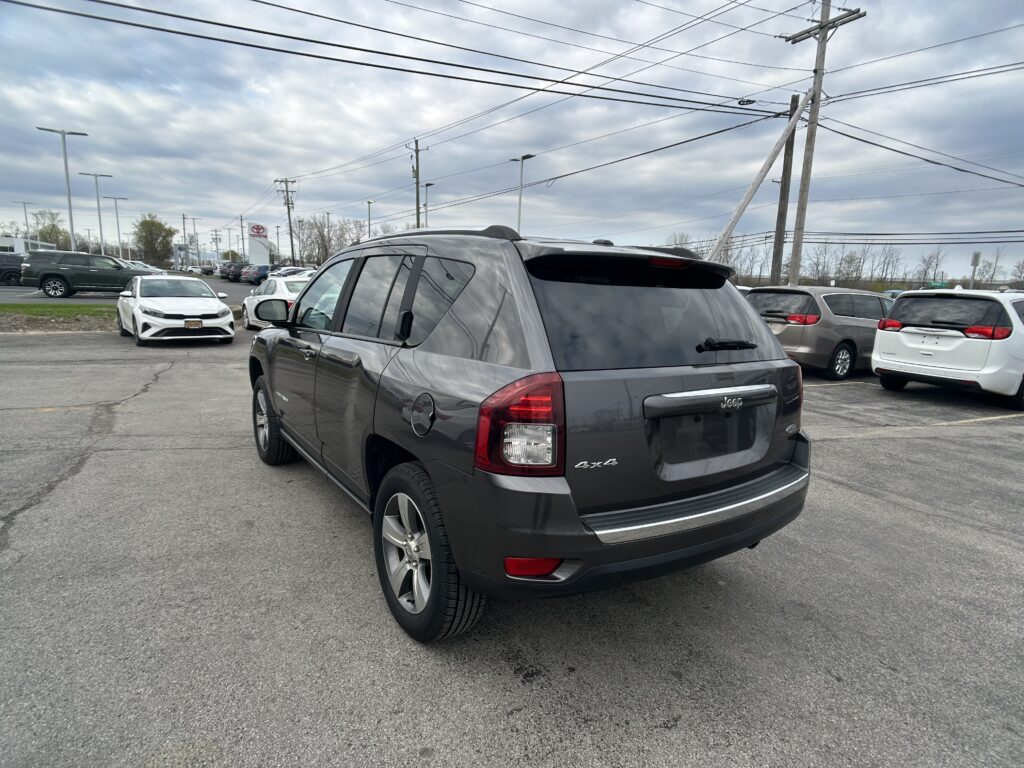 Rear three-quarter view of a gray Jeep SUV in a crowded parking lot, with power lines and a cloudy sky overhead.