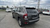 Rear three-quarter view of a gray Jeep SUV in a crowded parking lot, with power lines and a cloudy sky overhead.