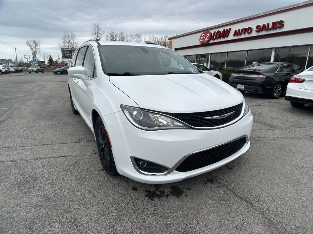 White Chrysler minivan in a dealership lot with EZ LOAN AUTO SALES building visible in the background and several parked cars nearby.