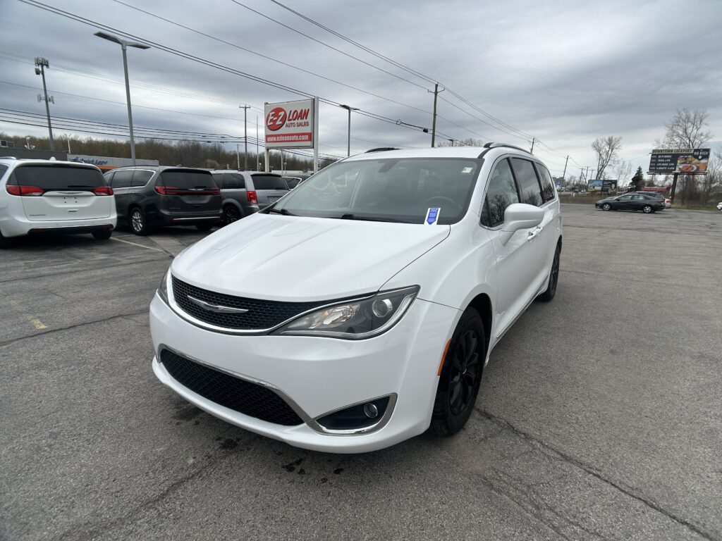 White SUV in a car lot with other vans, under a cloudy sky and an E-Z Loan Auto Sales sign nearby.