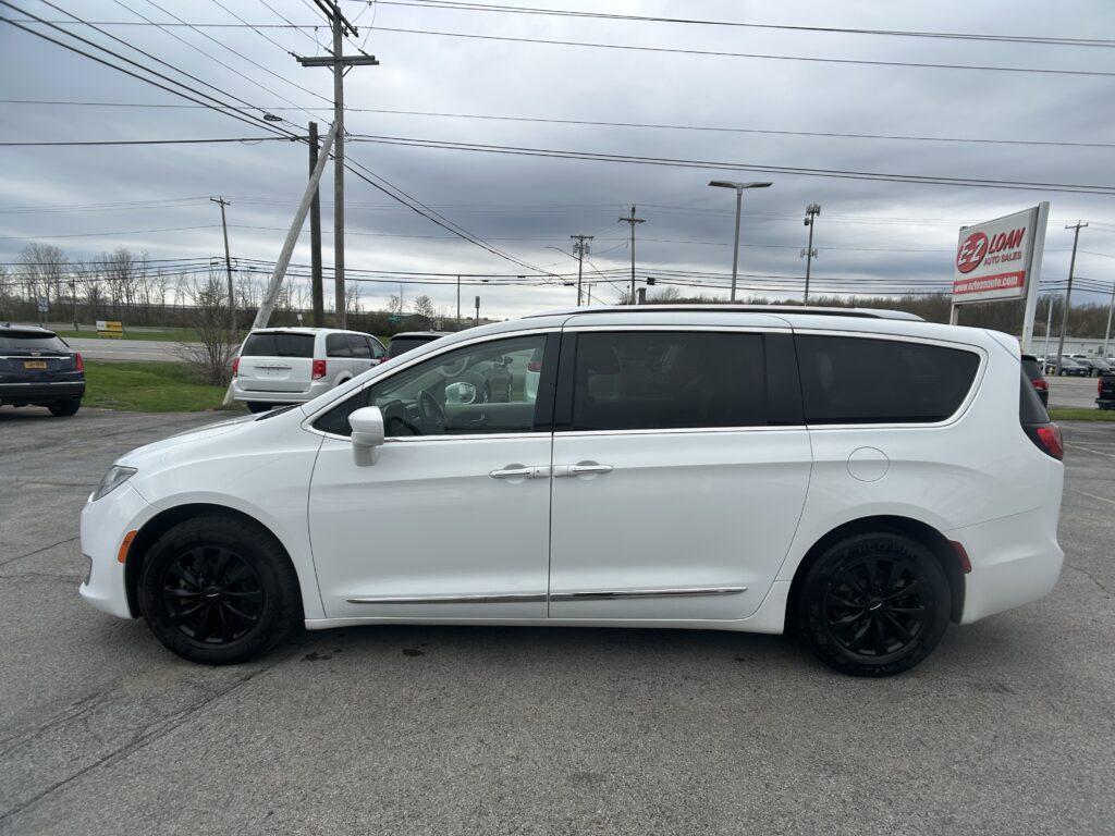 White minivan in a paved parking lot with a dealership sign and overcast sky in the background.