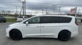 White minivan in a paved parking lot with a dealership sign and overcast sky in the background.