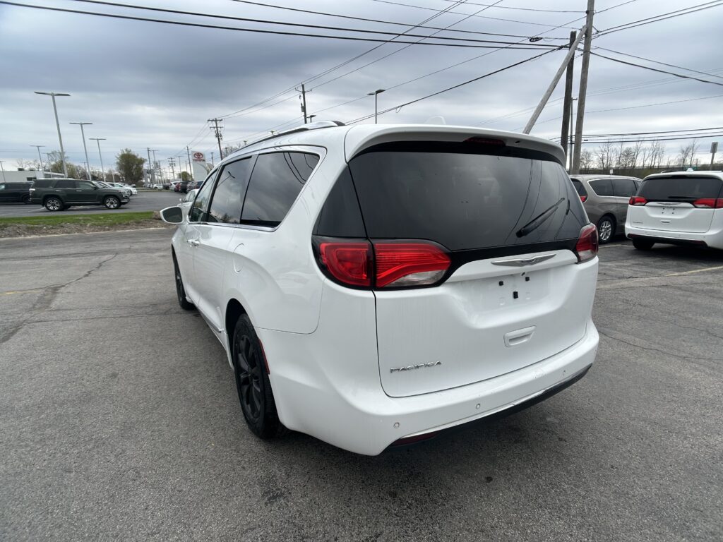 White minivan (Chrysler Pacifica) shown from the rear-right side in a parking lot with other vehicles and power lines overhead.