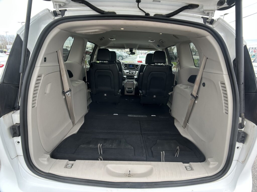 Open rear hatch showing a minivan's empty cargo area with folded third-row seats and black flooring, view toward the cabin designer interior.
