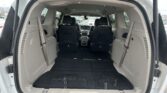 Open rear hatch showing a minivan's empty cargo area with folded third-row seats and black flooring, view toward the cabin designer interior.