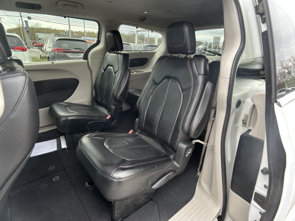 Interior of a vehicle showing black leather captain chairs in the second row, beige door panels, and a parking lot visible through the windows.