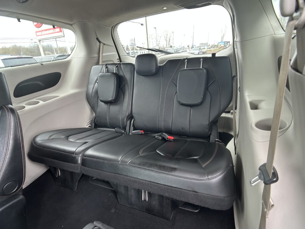 Black leather SUV rear seats with headrests, seat belts, and cupholders, view of parking lot through side windows