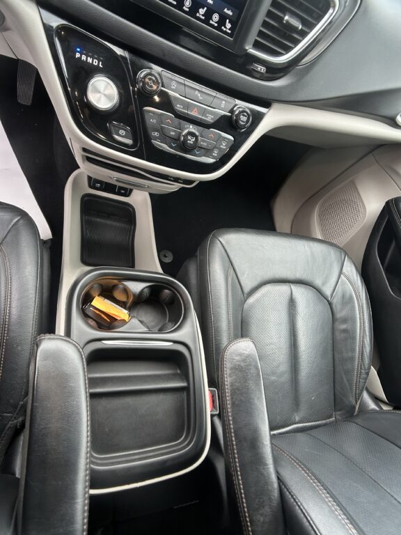 Center console of a car with cup holders, storage area, and gear selector visible between leather seats.
