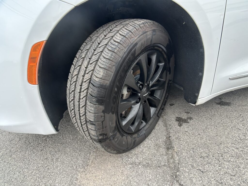 Close-up of a car’s front left wheel and tire with the orange side marker on the fender nearby.