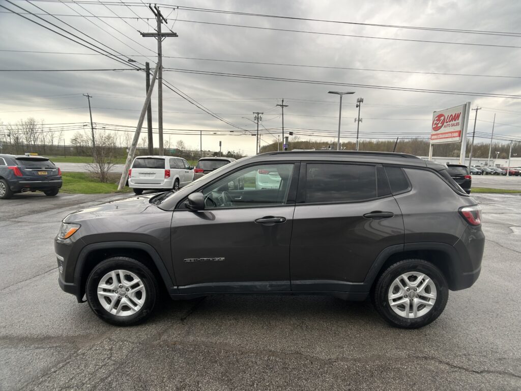 Dark gray Jeep Compass SUV parked in a lot, with a utility pole and overhead power lines in the background.