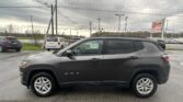 Dark gray Jeep Compass SUV parked in a lot, with a utility pole and overhead power lines in the background.