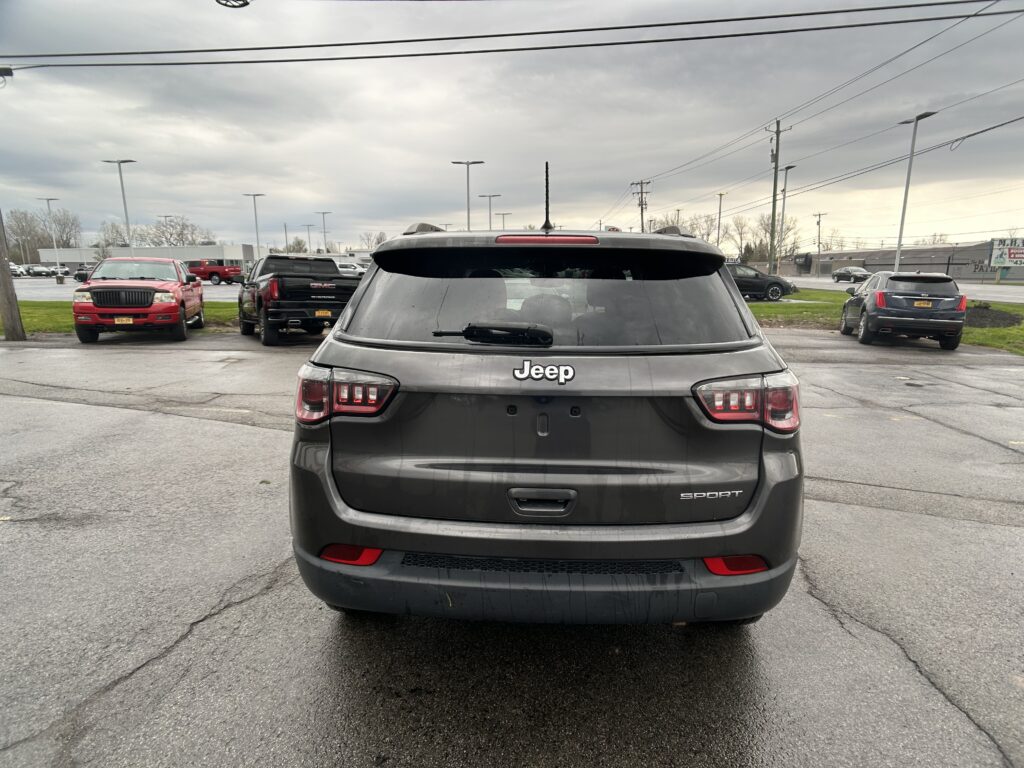 Rear view of a gray Jeep SUV in a parking lot under a cloudy sky; other cars are parked nearby and power lines are overhead.", "Dark gray Jeep SUV with SPORT badge, center of frame, surrounded by red and black vehicles in a lot on an overcast day.", "Rear of a Jeep Grand Cherokee-style SUV, showing taillights and rear window wiper, in a multi-car parking lot with a cloudy sky.", "Parking lot scene with several vehicles; main focus is the back of a gray Jeep SUV.", "Overcast day, center of image is a gray Jeep SUV’s rear end, with other cars and power lines in the background."]} }```Oops, there is an extra quote and formatting issue. Let's correct. I'll provide clean JSON.Oops. Provide corrected.`````````````````````````````თბილის?''` (Let's fix). I'll deliver proper JSON:```json{