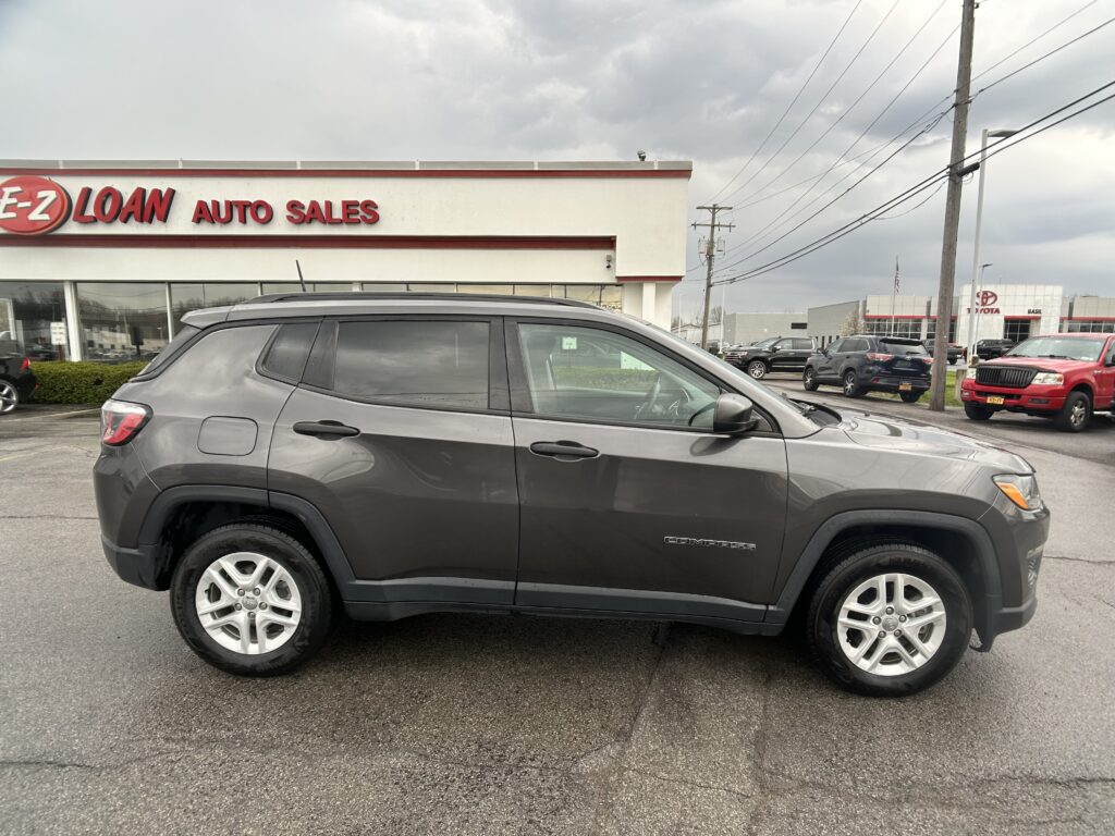 Gray Jeep Compass SUV parked in front of a used-car dealership with an "EZ LOAN AUTO SALES" sign on the building