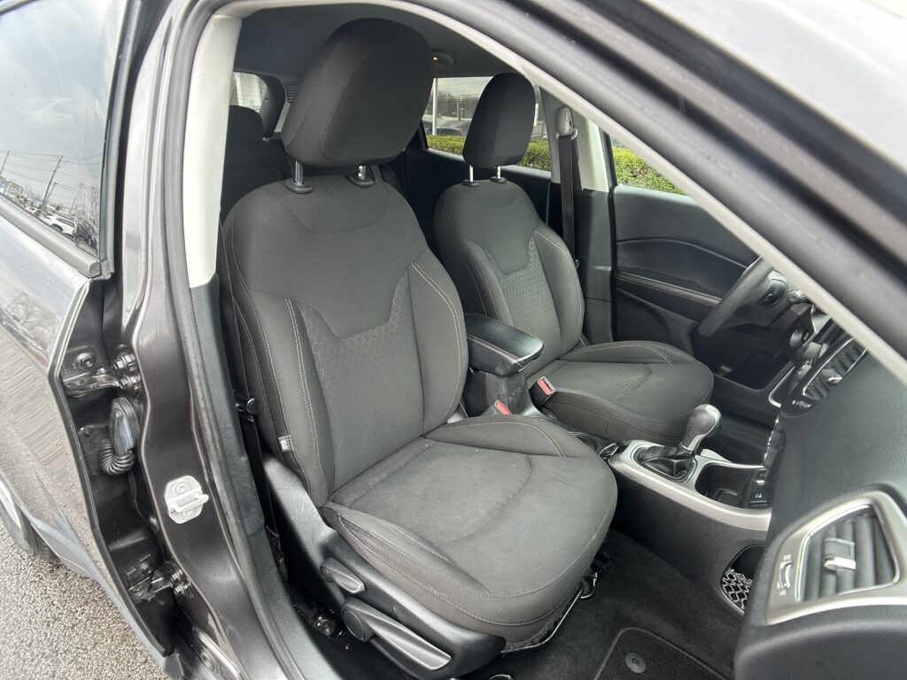 Right-hand-drive car interior showing two black fabric front seats with headrests, center console with armrest, gear shifter, and passenger-side door with seat belt visible.