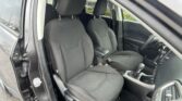 Right-hand-drive car interior showing two black fabric front seats with headrests, center console with armrest, gear shifter, and passenger-side door with seat belt visible.