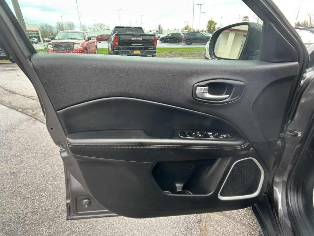 Close-up of a car's black door panel with window controls and door handle; outside a parking lot with trucks visible through the window.