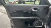 Close-up of a car's black door panel with window controls and door handle; outside a parking lot with trucks visible through the window.
