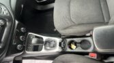 Interior of a car showing center console with gear shift, cup holder containing a small yellow item, and climate controls beside fabric seats with orange stitching.