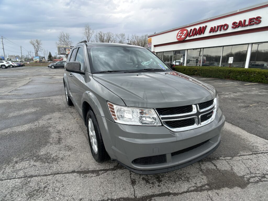 Front of a gray Dodge SUV parked in a dealership lot with a white building and red EZ LOAN AUTO SALES sign in the background.