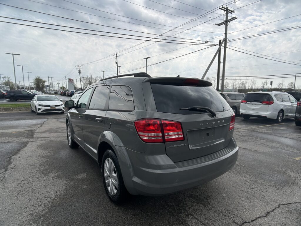 Rear view of a gray Dodge Journey SUV in a crowded car lot with power lines overhead, overcast sky above.