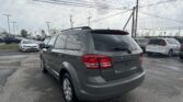 Rear view of a gray Dodge Journey SUV in a crowded car lot with power lines overhead, overcast sky above.
