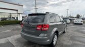 Gray Dodge SUV in a dealership parking lot with a white building on the left and power lines across a cloudy sky.