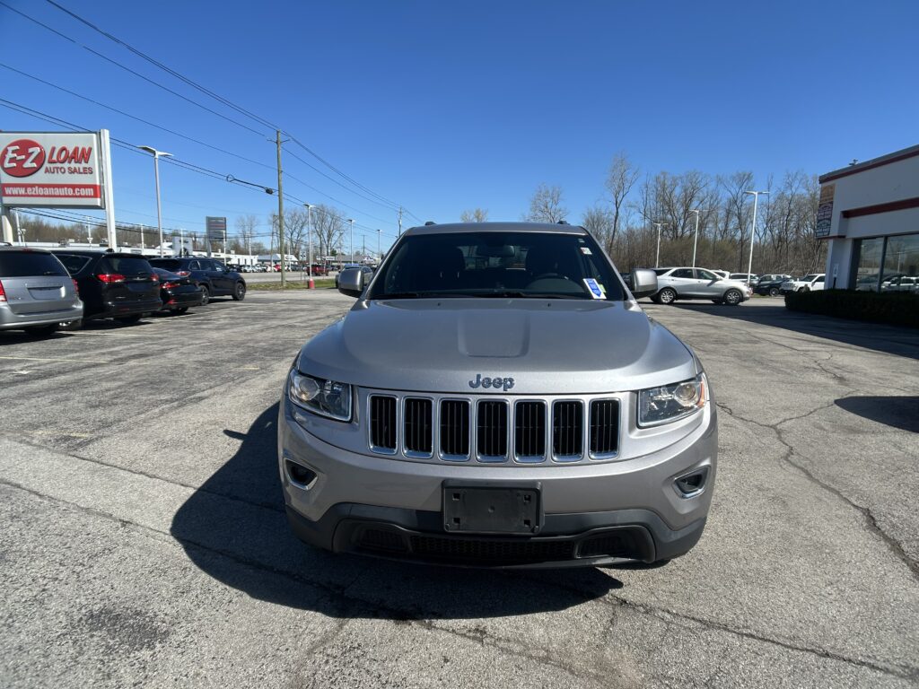 Front view of a silver Jeep SUV in a busy car dealership lot with other vehicles and an EZ LOAN Auto Sales sign on the left under a clear blue sky