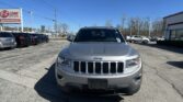 Front view of a silver Jeep SUV in a busy car dealership lot with other vehicles and an EZ LOAN Auto Sales sign on the left under a clear blue sky