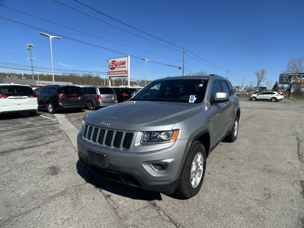 Silver SUV in a dealership lot foreground with an EZ Loan Auto Sales sign against a blue sky, rows of cars behind it.