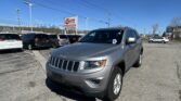 Silver SUV in a dealership lot foreground with an EZ Loan Auto Sales sign against a blue sky, rows of cars behind it.