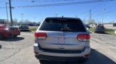 Rear view of a silver Jeep SUV in a parking lot with other cars and clear blue sky above, power lines overhead.
