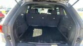Open SUV rear hatch showing empty cargo area with three-row seats upright and a black rubber mat; parking lot in the background.