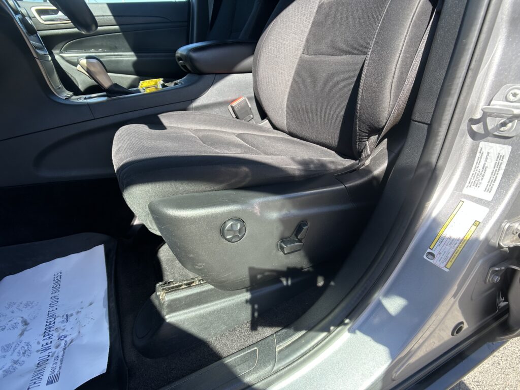 Front passenger seat in a dark car interior with center console and door panel visible, plus a warning label on the door frame edge.