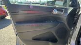 Interior of a car door with window controls and chrome handle; parking lot visible through the open door on a sunny day