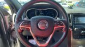Close-up of a Jeep steering wheel and dashboard, with a sunny parking lot visible through the windshield readout over the instrument cluster.