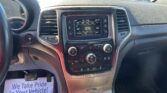 View of a car's dashboard from the driver’s seat: center touchscreen shows radio and climate controls, with parked cars visible through the windshield.
