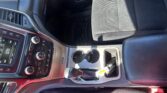 Interior view of a car's front cabin: center console with gear selector, cup holders, and climate/control dials, plus black fabric seats and dashboard details visible.