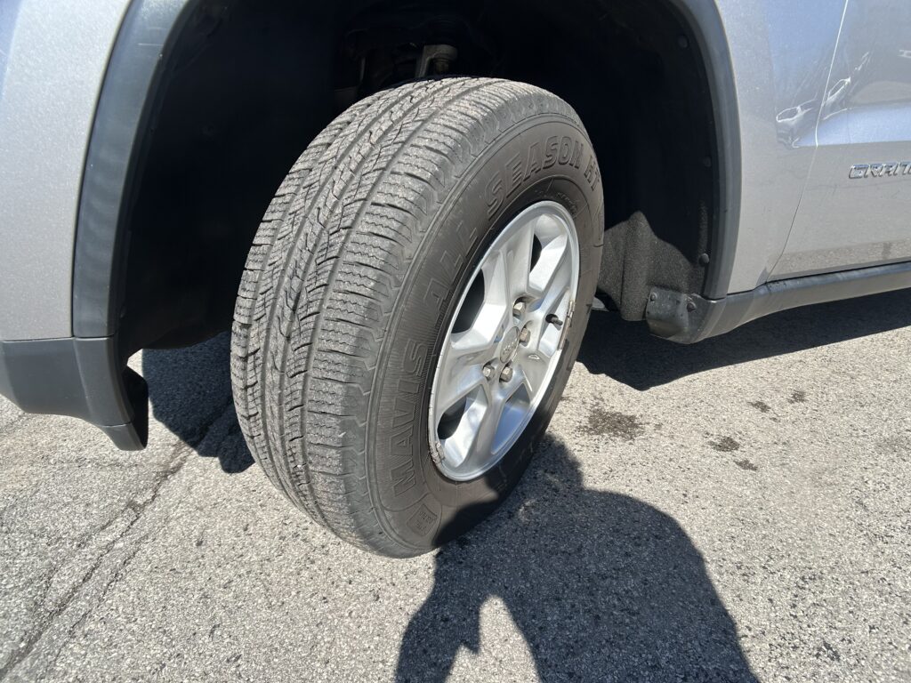 Close-up of a silver SUV wheel with an all-season tire; wheel well and fender visible.