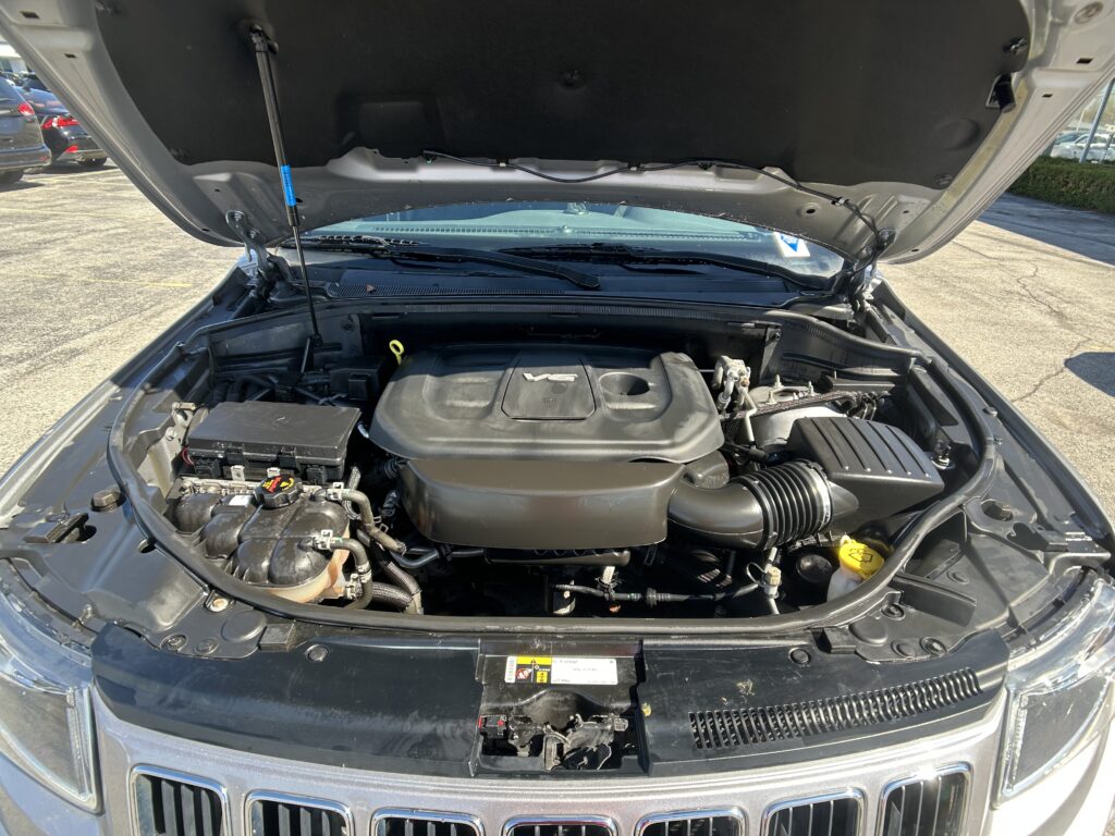 Under-hood view of a vehicle with the hood raised, showing the engine bay, battery, and air intake hose.
