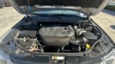 Under-hood view of a vehicle with the hood raised, showing the engine bay, battery, and air intake hose.