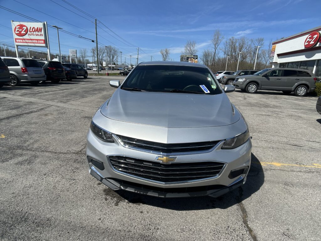 Silver Chevrolet car in a dealership lot with E-Z LOAN Auto Sales signs visible in the background, blue sky overhead.
