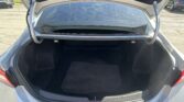 Open trunk of a dark sedan showing an empty cargo area with a black carpeted floor mat and rear seats nearby.