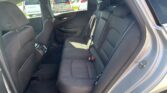 Rear interior of a dark cloth car with three headrests and seatbelts, door panel visible on the left, parked cars outside through the window.