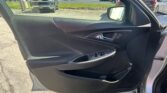 Close-up of a black car door panel with window controls, viewed from inside; outside is a dealership lot with trucks and cars in the background.