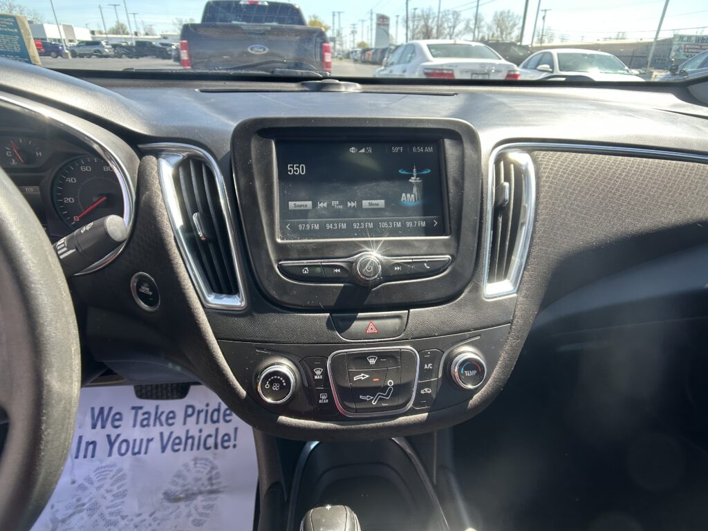 Driver's-seat view of the dashboard with a center touchscreen showing 550 AM and climate controls, plus a 'We Take Pride In Your Vehicle!' flyer on the floor.